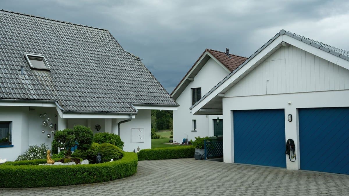 Gepflasterte Zufahrt zwischen zwei Wohnhäusern, die zu Garagen im hinteren Grundstücksbereich führt