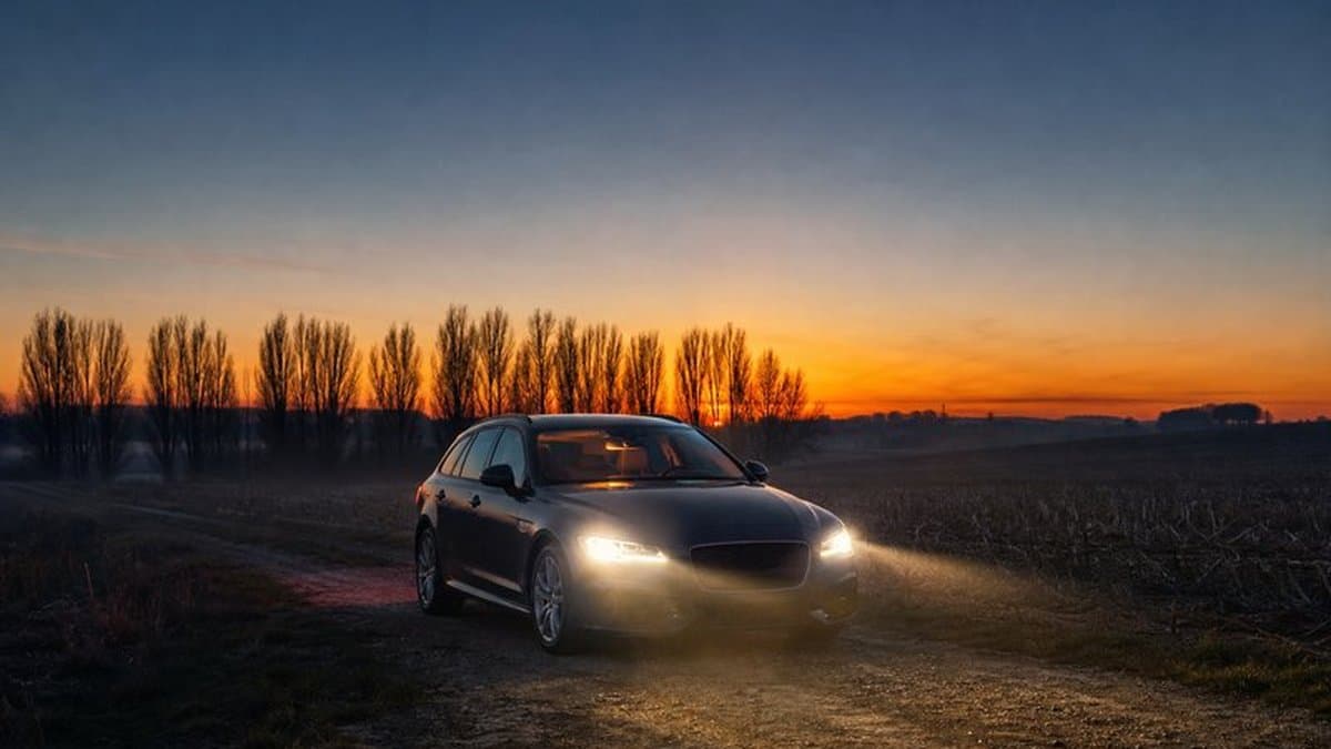Auto mit eingeschalteten Scheinwerfern steht in der Dämmerung auf einem Feldweg neben einem abgeernteten Feld
