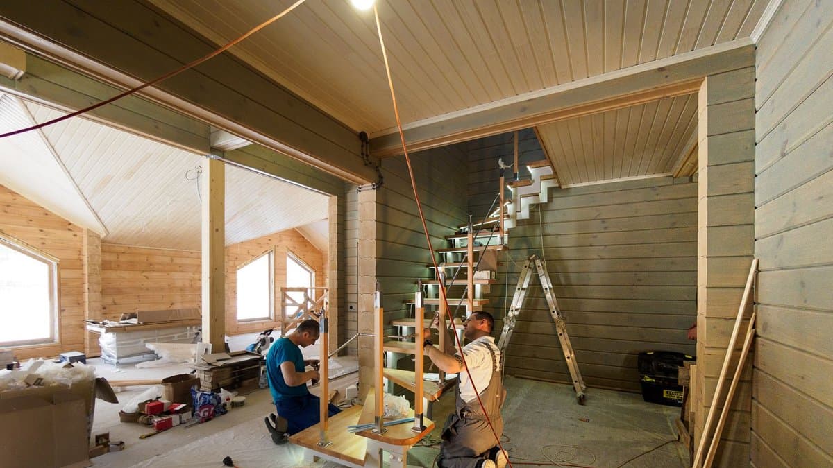 Zwei Handwerker montieren eine Holztreppe im Inneren eines neu gebauten Holzhauses