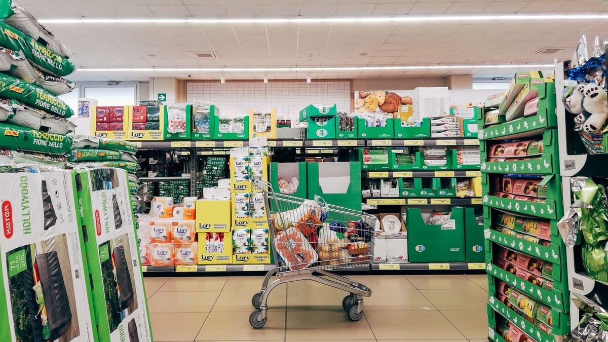 Einkaufswagen steht allein in einem Gang zwischen Supermarktregalen