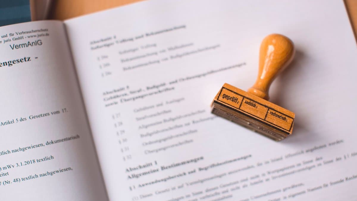 Aufgeschlagenes Gesetzbuch auf einem Schreibtisch, daneben ein Holzstempel