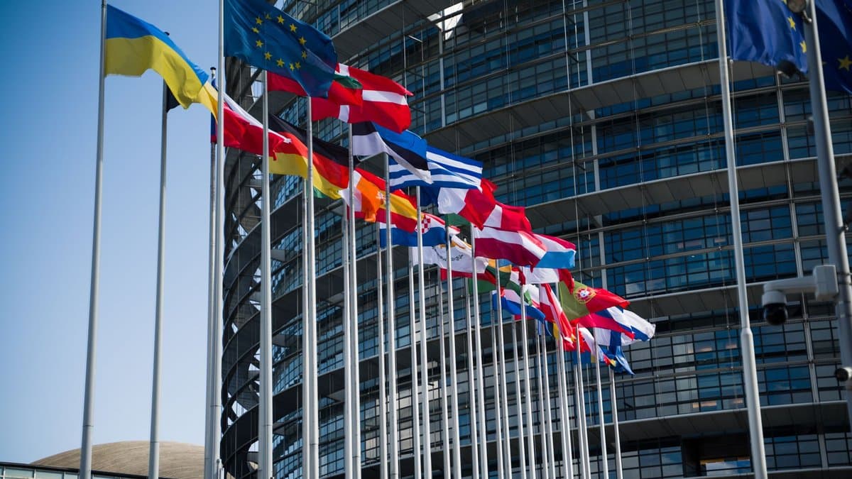 Flaggen der EU-Mitgliedstaaten wehen vor der gewölbten Glasfassade des Europäischen Parlaments