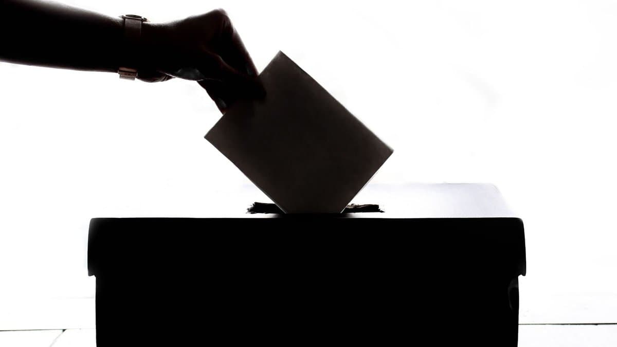 Silhouette einer Hand, die einen Stimmzettel in eine Wahlurne wirft