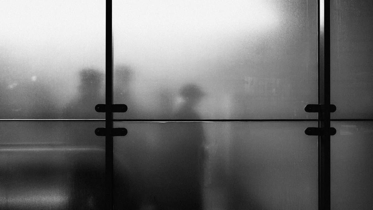 Schemenhafte Gestalten hinter einer Milchglaswand, eine Person mit Hut in der Mitte