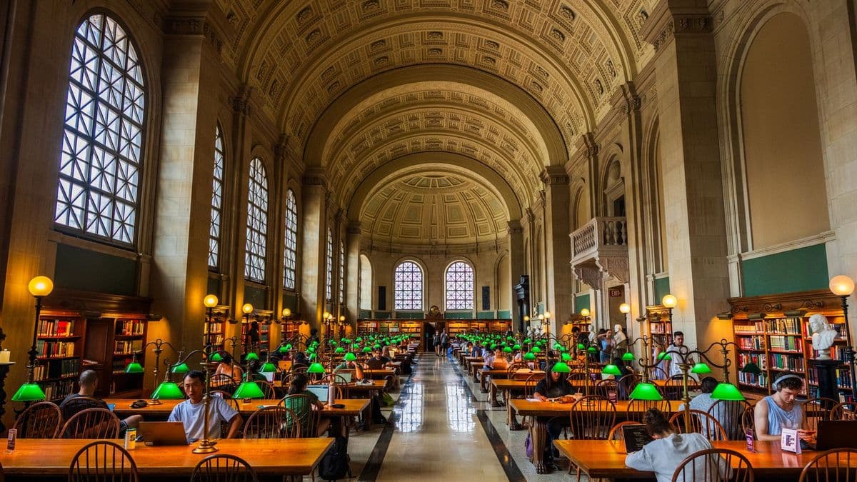 Weiter Bibliothekslesesaal mit langen Holztischen, grünen Leselampen und lernenden Studierenden