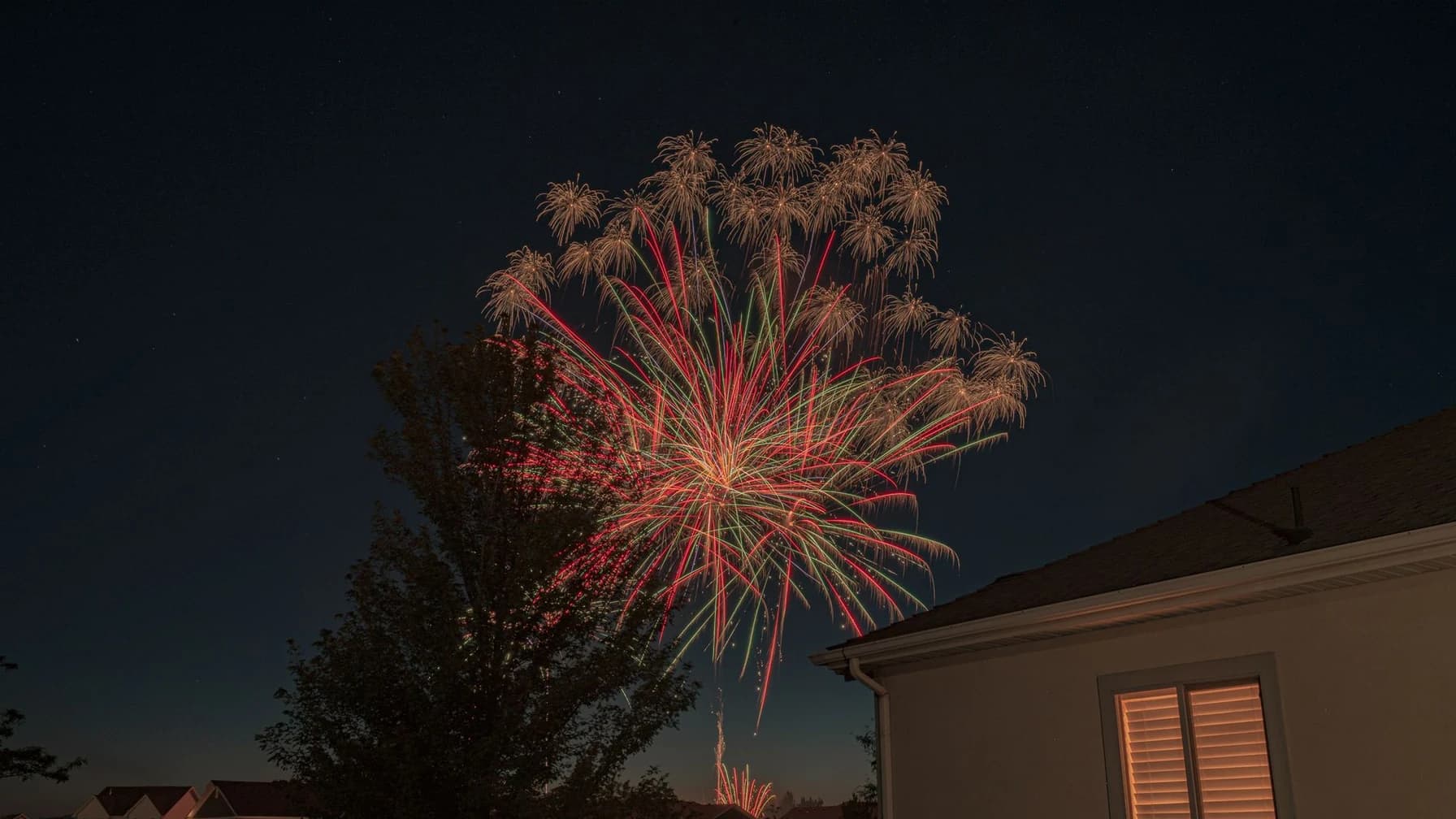 Buntes Feuerwerk am Nachthimmel über den Dächern einer Wohnsiedlung