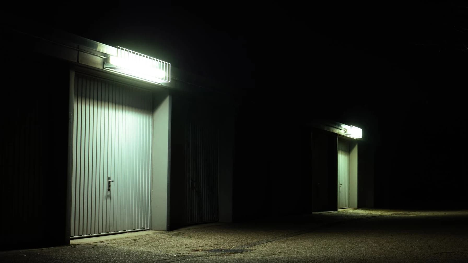 Nächtliche Wohnstraße mit zwei baugleichen, beleuchteten Garagentoren nebeneinander