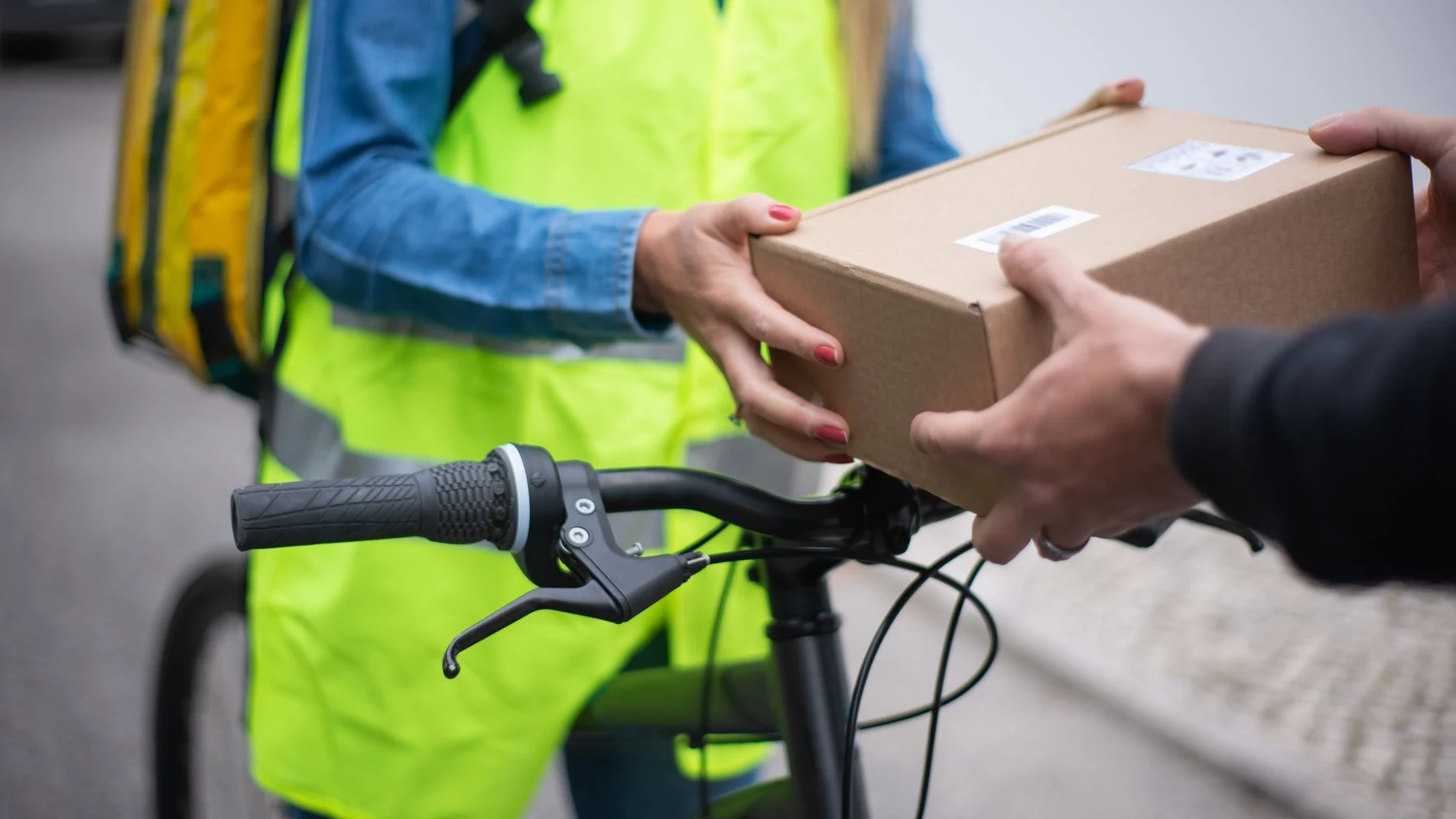 Eine Person übergibt einem Kurier mit Warnweste einen Paketkarton