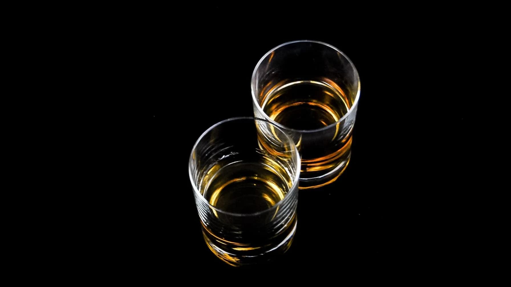 Zwei Whiskygläser mit Eis auf einer dunklen, spiegelnden Bartheke