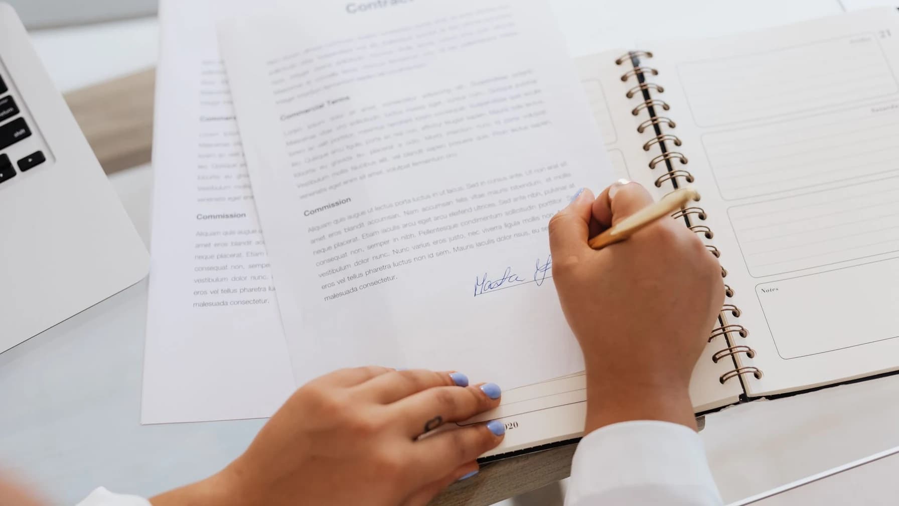 Hand unterschreibt ein Vertragsdokument auf einem Schreibtisch mit weiteren Unterlagen.
