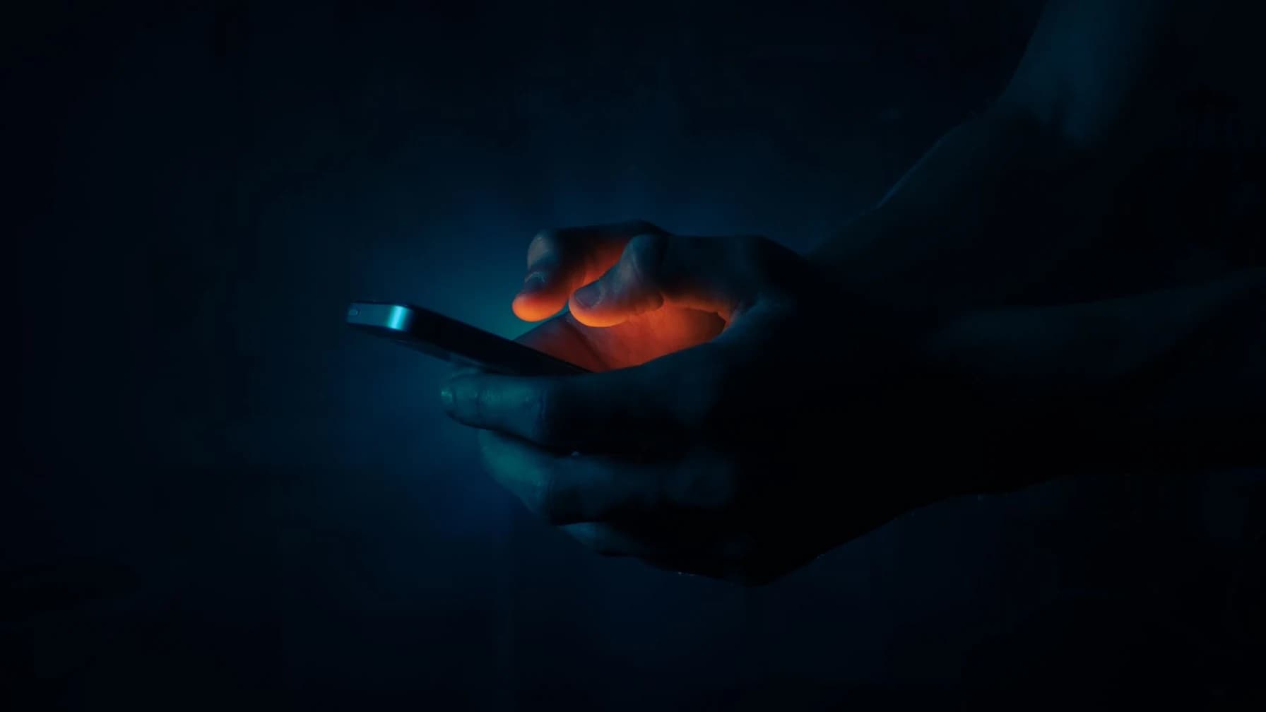 Eine Hand hält im Dunkeln ein leuchtendes Smartphone