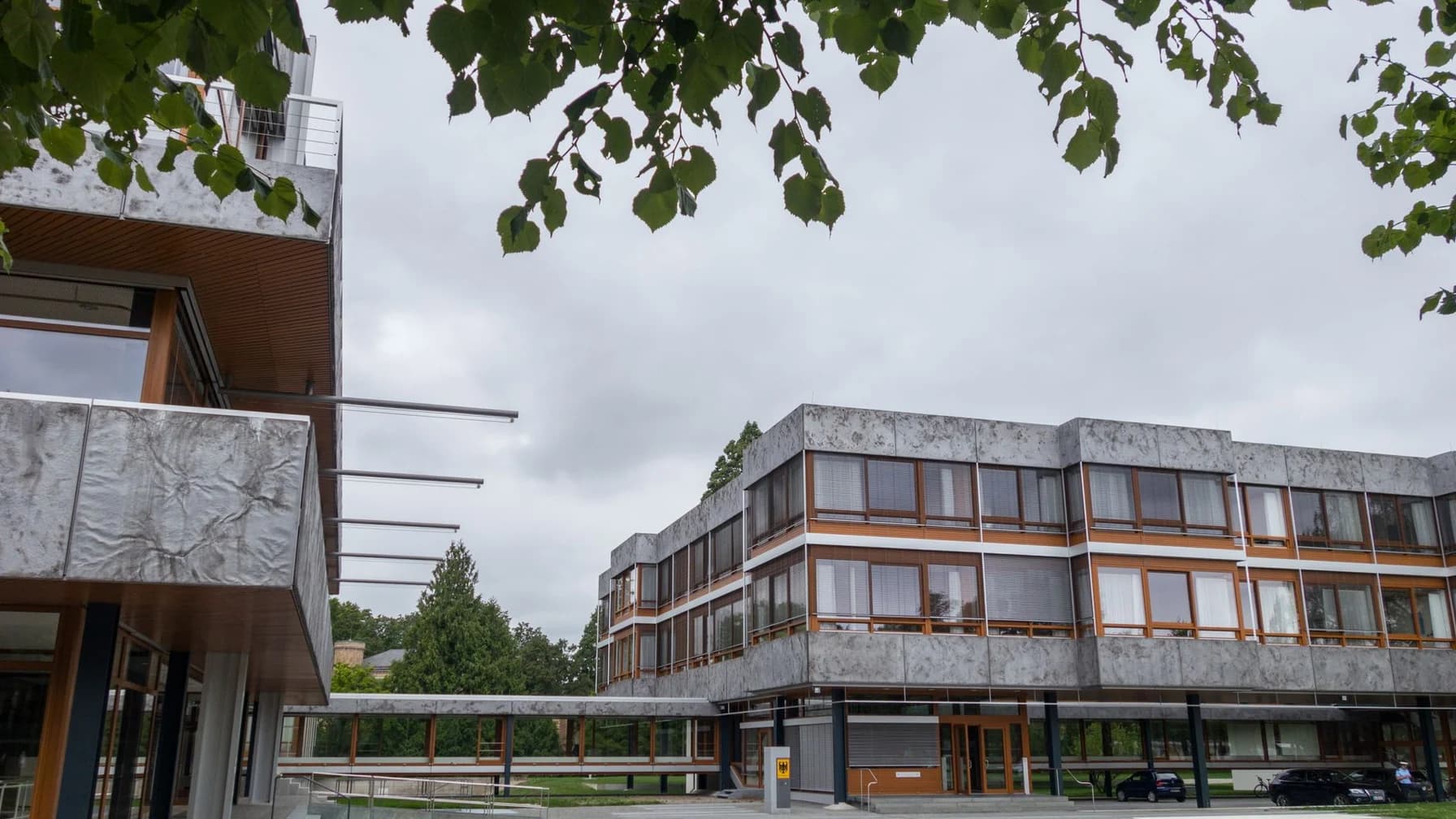 Gebäude des Bundesverfassungsgerichts in Karlsruhe unter bewölktem Himmel, Ansicht mit Bäumen im Vordergrund