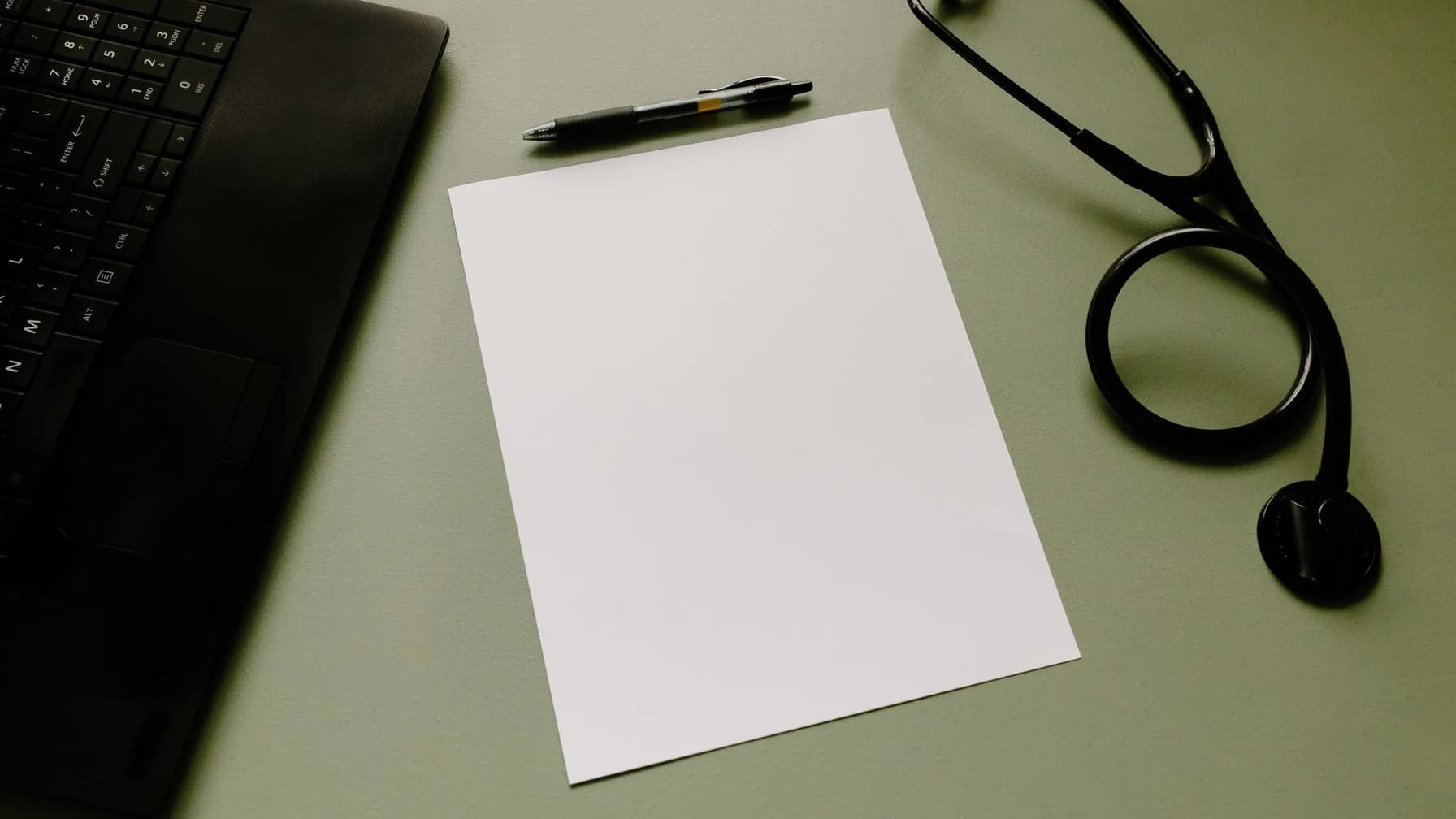 Stethoskop und ein leeres Formularblatt liegen neben einem Kugelschreiber auf einem Schreibtisch in einer Arztpraxis