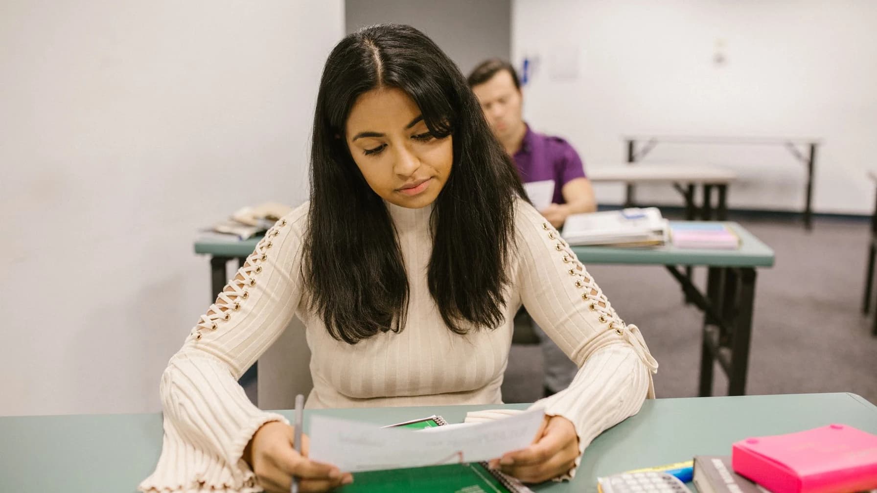 Junge Jurastudentin sitzt am Tisch und blättert nachdenklich in ihrer zurückgegebenen Hausarbeit