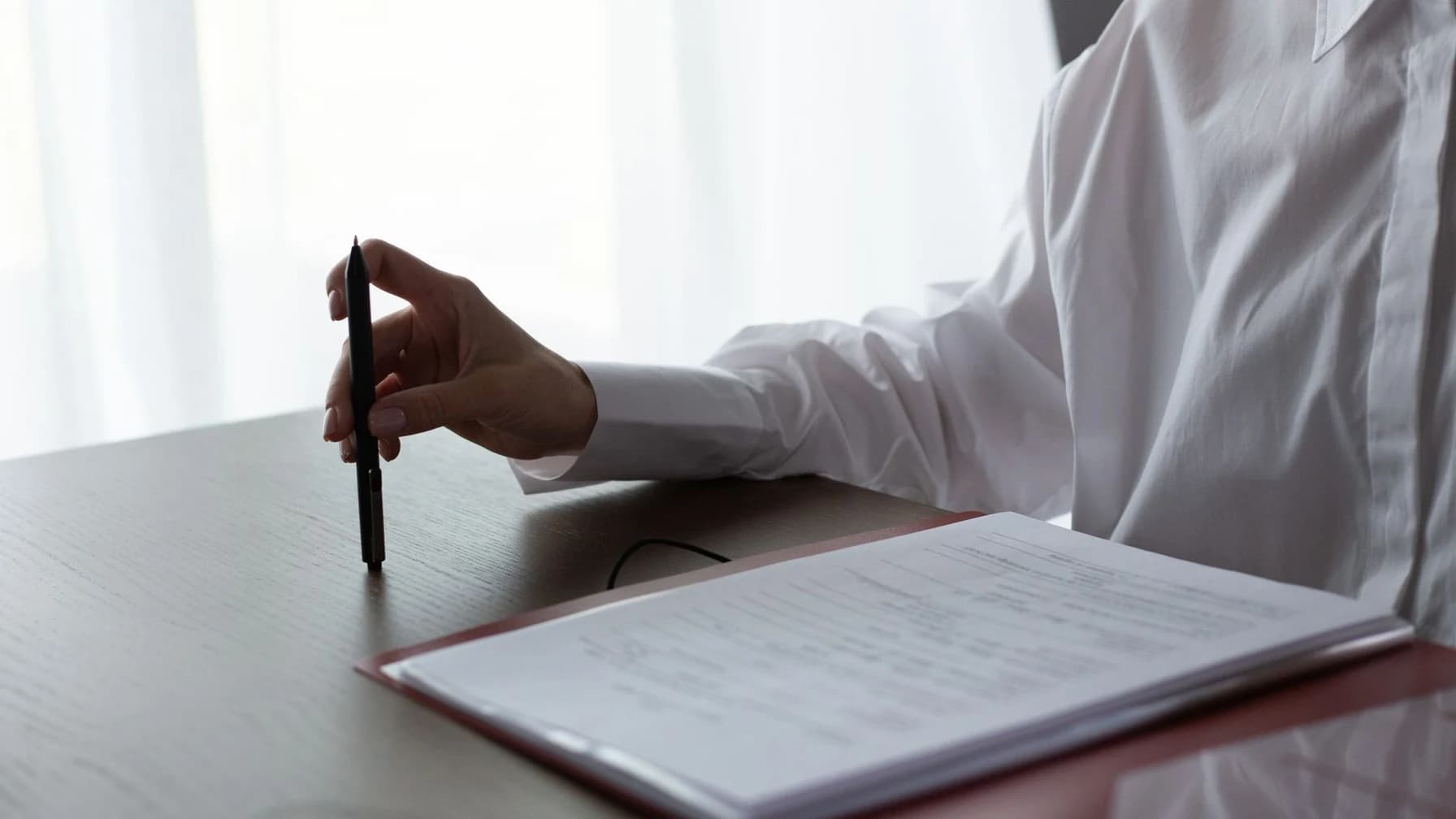 Person setzt an einem Schreibtisch mit einem Stift ein Schreiben zu einem Vertrag auf