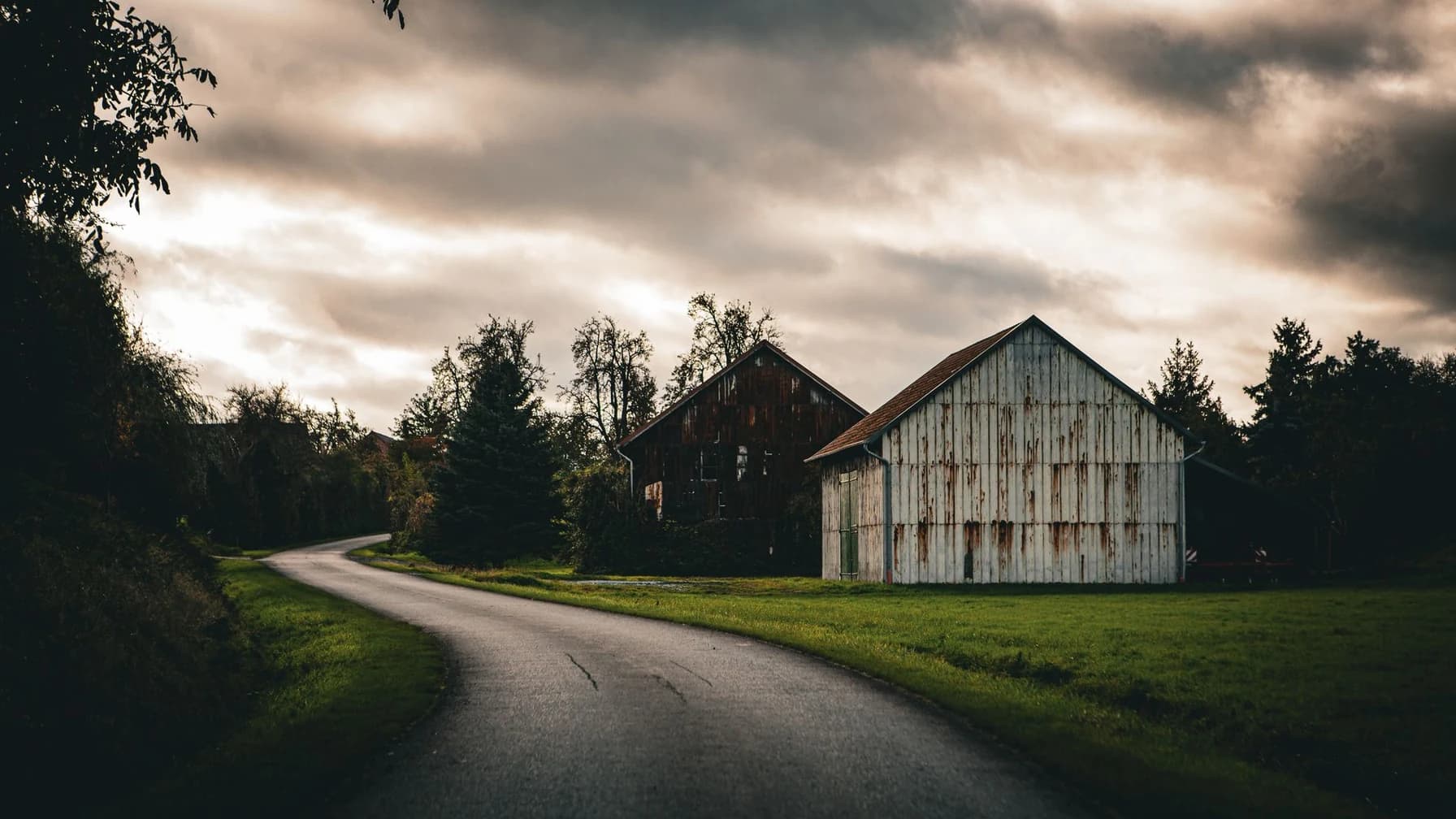 Landstraße führt in der Abenddämmerung an einem alten Gehöft mit Scheune vorbei
