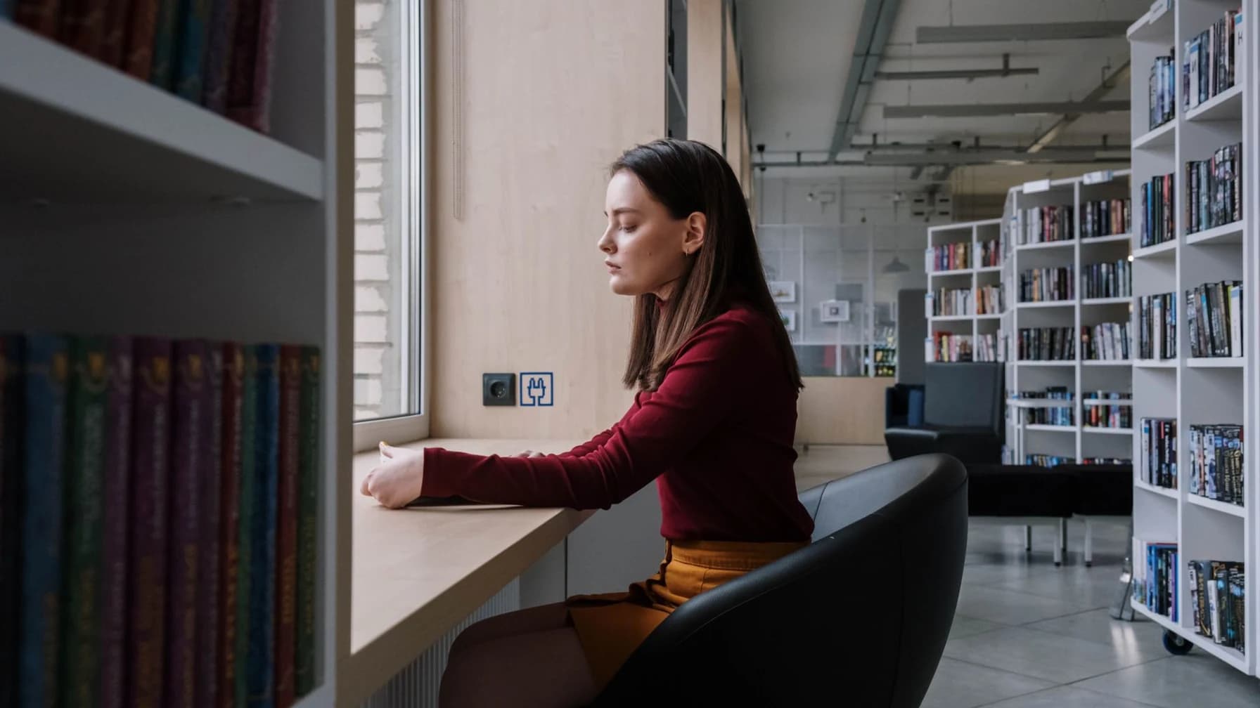 Jurastudentin sitzt gelassen an einem Fenstertisch im Lesesaal einer Bibliothek