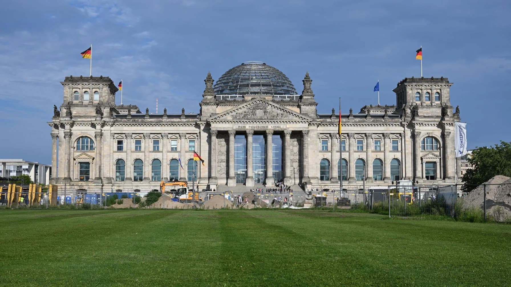 Das Reichstagsgebäude in Berlin mit Glaskuppel und Flaggen, davor eine Rasenfläche