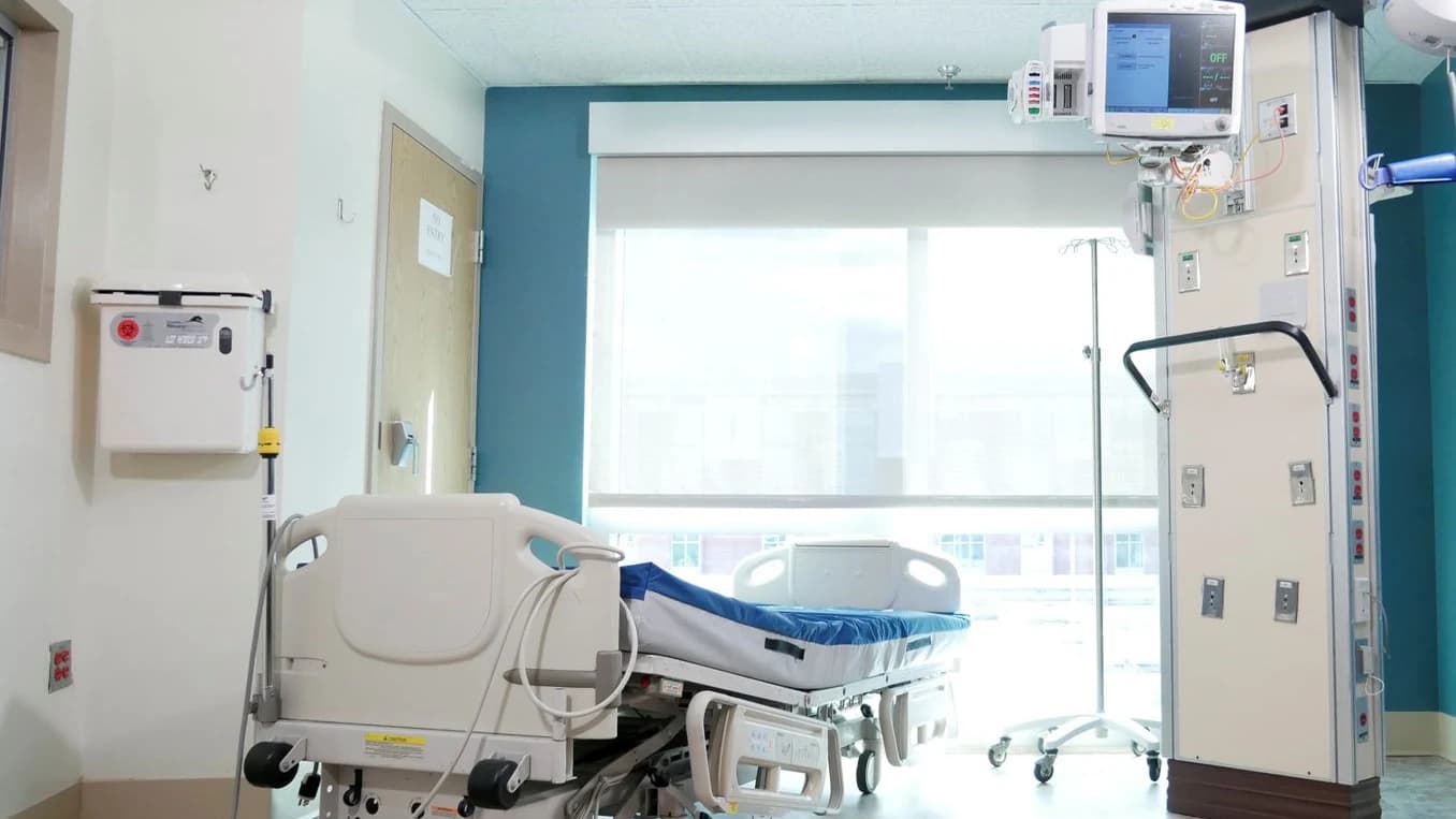 Leeres, ruhiges Krankenzimmer mit Bett vor einem hellen Fenster
